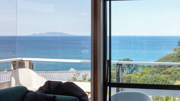 Quarto com uma janela ampla que oferece vista para o mar e terra ao longe.