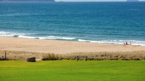 Uma praia com área gramada, um banco e o oceano ao fundo.