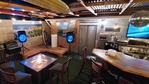 A bar area with a fire pit, wooden tables, and chairs. There are speakers and a television. - This Venue is set up for hourly rates only. 4.5 hour min.  Capacity 150 guests   (Costa Mesa)