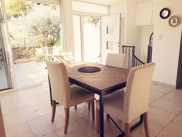 Un comedor con una mesa de madera y cuatro sillas, una alfombra pequeña y vista a un jardín por una puerta de cristal.