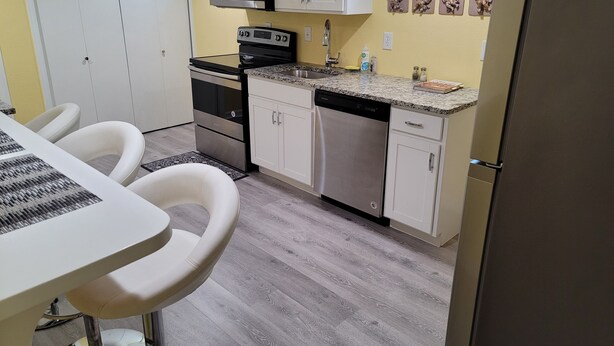A compact kitchen with white cabinets, a microwave, a stove, and a dishwasher. There is a dining area with a table and chairs. - In the Heart of Longmont ~ 15 Minutes to Boulder, Colorado (Longmont)