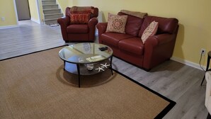 A living room with a glass coffee table, two red leather sofas, a patterned rug, and a staircase in the background. - In the Heart of Longmont ~ 15 Minutes to Boulder, Colorado (Longmont)