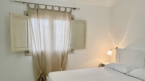 A bedroom with a bed, a nightstand, a lamp, and a window with curtains. - Mediterranean&sea Shell House (Limpiddu)