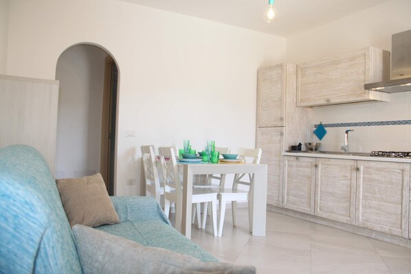 A modern kitchen with white cabinets, a dining table with chairs, and a blue sofa in the living area.