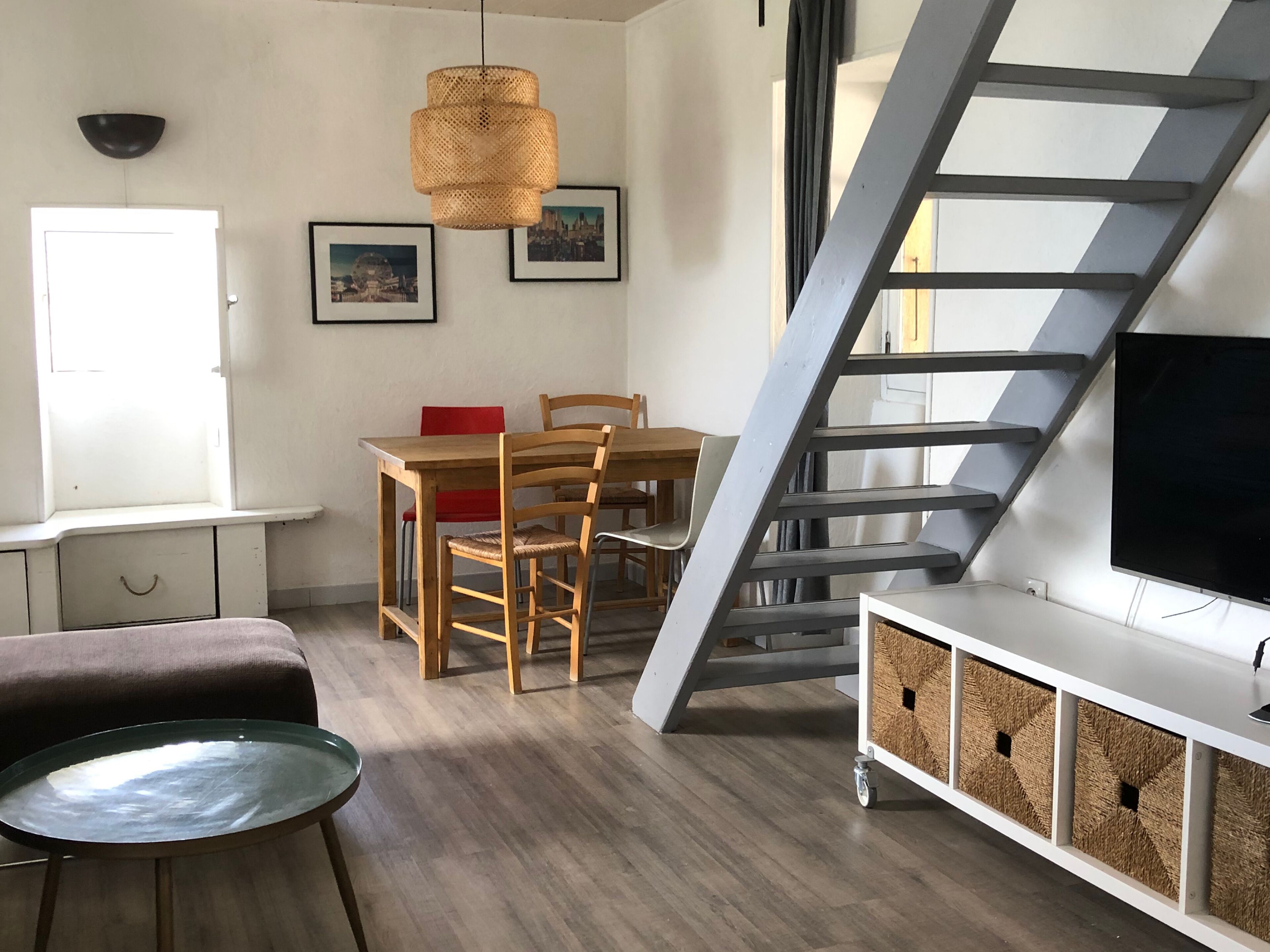 A modern living room with a dining area, a staircase, and a TV on a white cabinet.