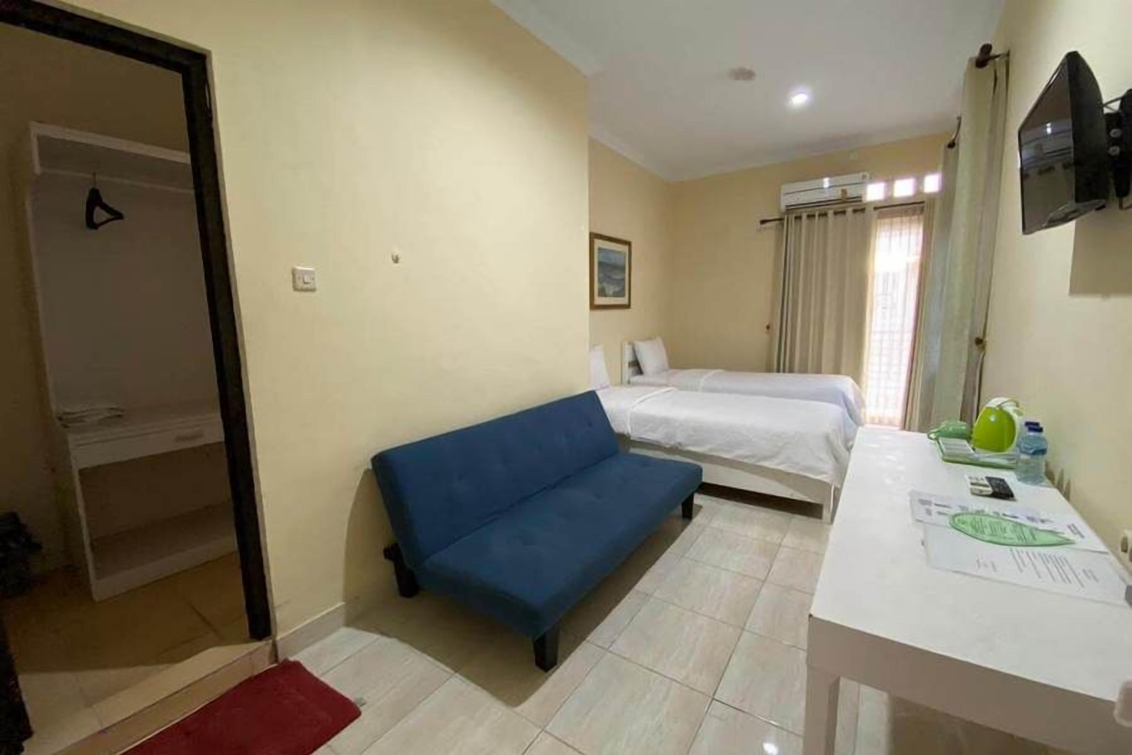 A room with a sofa, a bed, a desk with papers, and a TV on the wall.