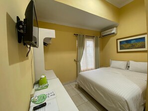 Una camera d'albergo con un letto, una scrivania con un telefono e un oggetto verde, un quadro al muro e un condizionatore d'aria.