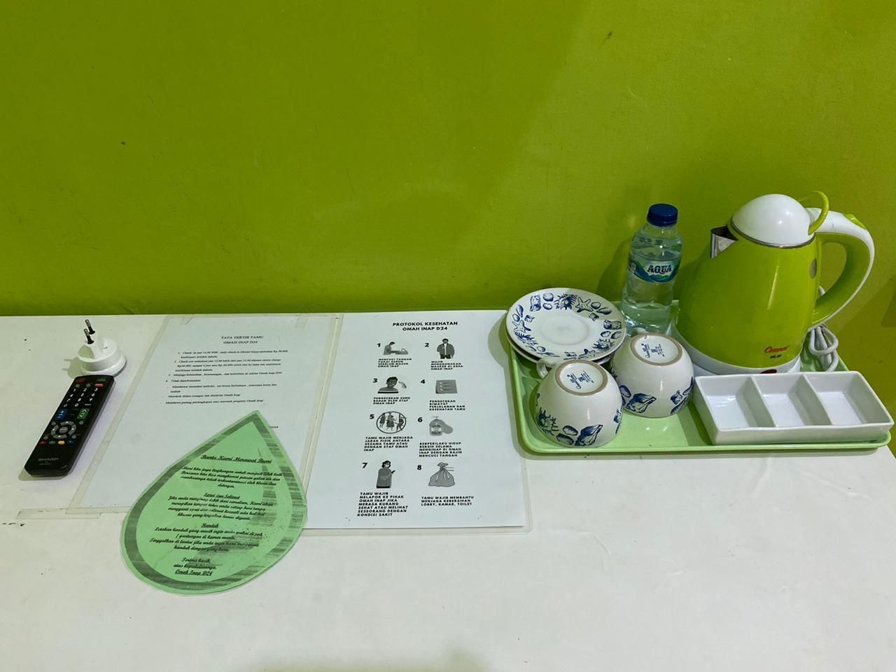 Une table avec une télécommande, une théière verte, une bouteille d’eau, un plateau avec des tasses et un menu.