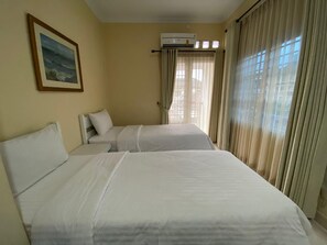 A hotel room with two beds, a painting on the wall, an air conditioning unit, and curtains on the windows. - Omah Inap D24 Syariah Near Universitas Aisyiah Yog (Sleman)