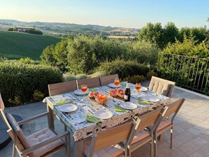 An outdoor dining table set with plates, glasses, and a bottle, surrounded by chairs, with a scenic view in the background. - Ostra Villa - Sleeps 8 - Pool - Garden - Parking (Ostra)