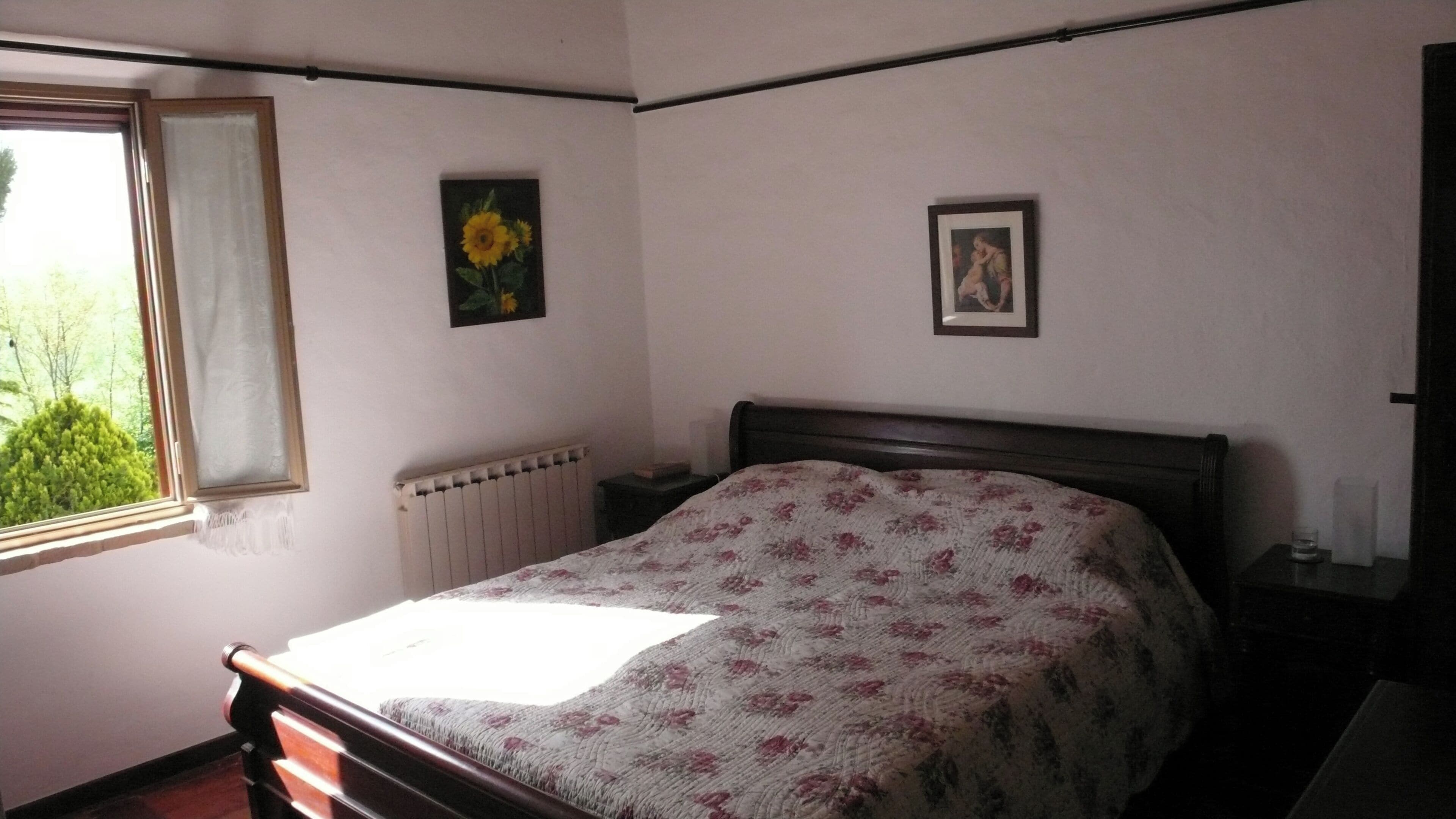 Un dormitorio con cama, ventana, radiador y dos cuadros en la pared.