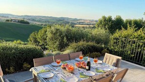 An outdoor dining table set with plates, glasses, and a bottle, surrounded by chairs, with a scenic view in the background. - Ostra Villa - Sleeps 8 - Pool - Garden - Parking (Ostra)