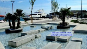 A seafront promenade with concrete planters and seating areas, a yacht docked nearby, and a clear view of the sea.