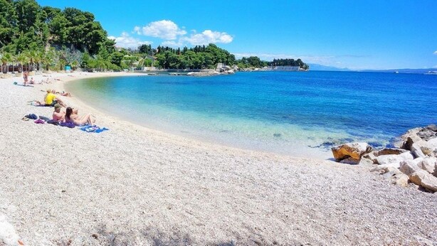 A beach with pebbles, people sunbathing, and a clear blue sea.