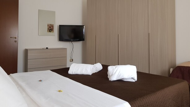 A hotel room with a bed, a TV mounted on the wall, a wardrobe, and a door. - Appartamento Le Campane (Verona)
