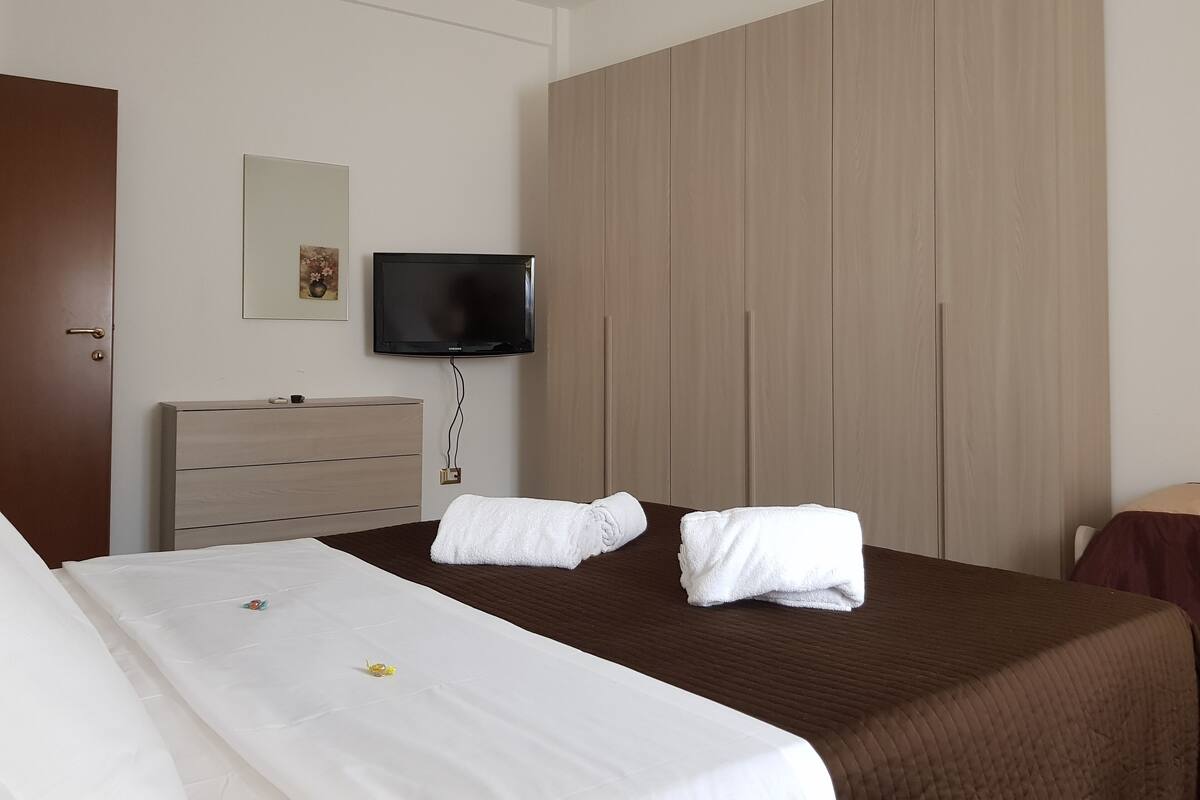 Habitación de hotel con cama, televisión montada en la pared, armario y puerta.