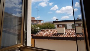 A view through a window of a building with a tiled roof and a clear sky with clouds. - Appartamento Le Campane (Verona)