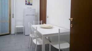 A small, clean room with a white table and chairs, a refrigerator, a clock, and a door. - Appartamento Le Campane (Verona)