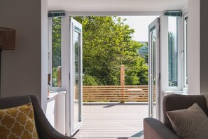 Un balcón abierto con cubierta de madera, vistas a árboles y valla de madera.