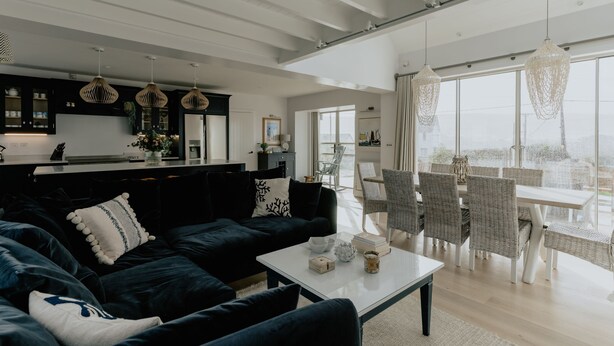 A modern living room with a dark sofa, white coffee table, and wicker chairs. - The Old Coastguards, Sleeps 8, Pets, Hot Tub (Braunton)