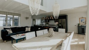 A modern living room with a dark sofa, a white coffee table, and a dining table with woven chairs. - The Old Coastguards, Sleeps 8, Pets, Hot Tub (Braunton)