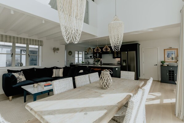 A modern living room with a dark sofa, a white coffee table, and a dining table with woven chairs.