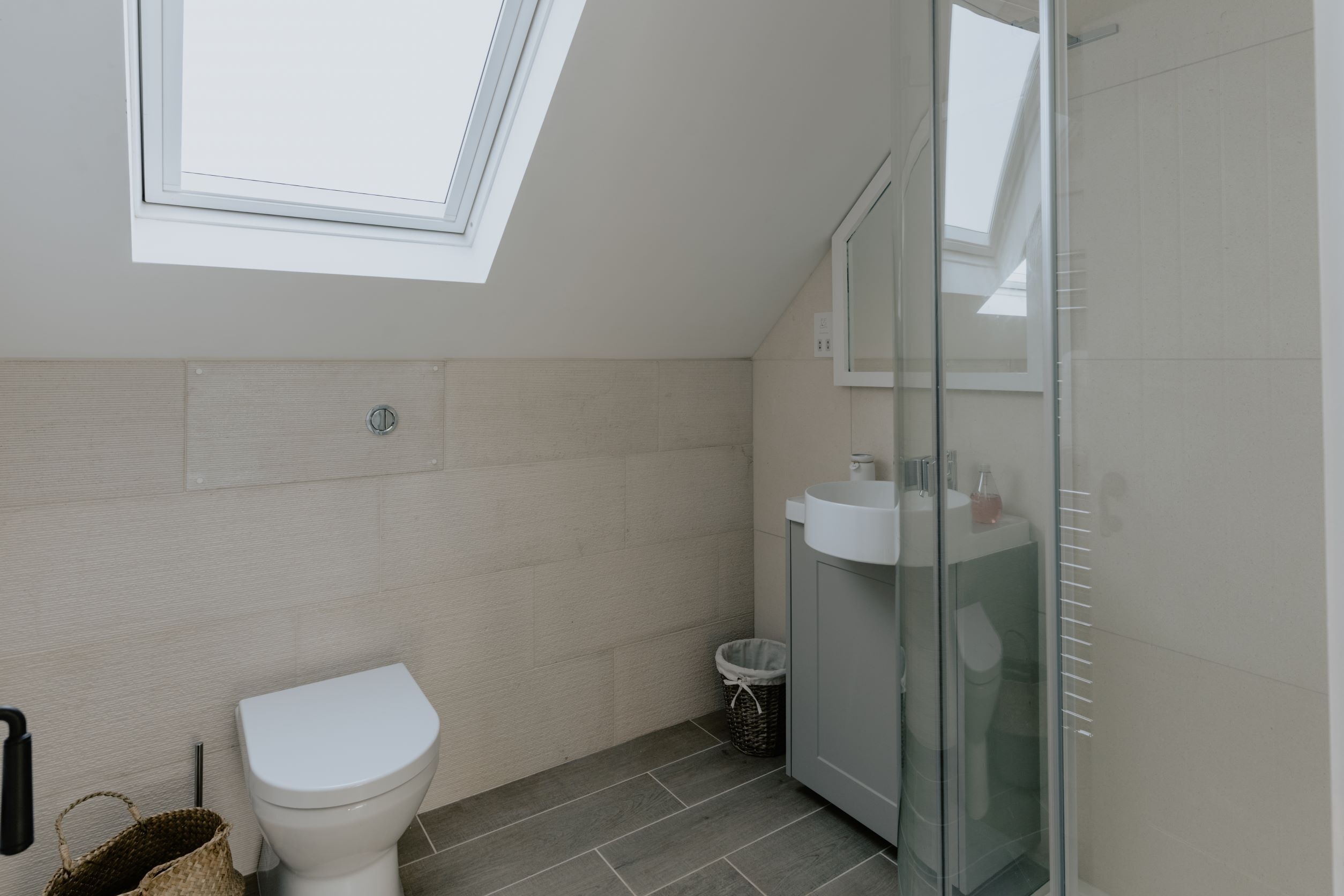 A modern bathroom with a skylight, a toilet, a glass shower enclosure, and a sink.