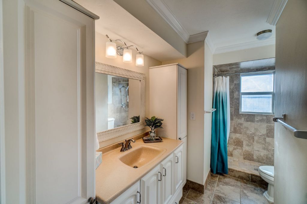 Une salle de bain avec un lavabo beige, des meubles blancs, un grand miroir et un rideau de douche.