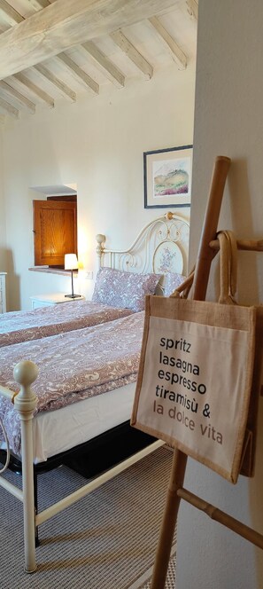 A bedroom with a bed, a wooden headboard, a nightstand, a lamp, a framed picture on the wall, and a tote bag with text. - Passiontoscane : house with private pool, breathtaking view and total confort (San Giovanni d'Asso)