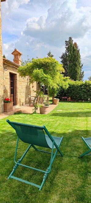 A stone building with a chimney, a grassy yard, and a pergola with climbing plants. - Passiontoscane : house with private pool, breathtaking view and total confort (San Giovanni d'Asso)