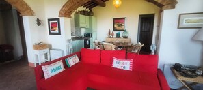 A cozy living room with a red sofa, a dining table with chairs, and a kitchen in the background.