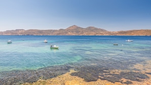 A coastal scene with clear turquoise water, rocky shoreline, and boats. - The Colourful Land Klima, Milos (Klima)