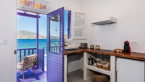 A compact kitchen with a view of the sea, a small dining area with a chair, and a purple door leading to an outdoor balcony. - The Colourful Land Klima, Milos (Klima)