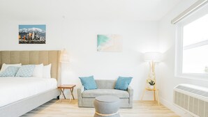 A modern hotel room with a bed, a grey sofa, a round ottoman, a small table, and a lamp. There are two paintings on the wall. - SKS - Superior Room, 1 King Bed with Sofa bed, Non Smoking (Long Beach)