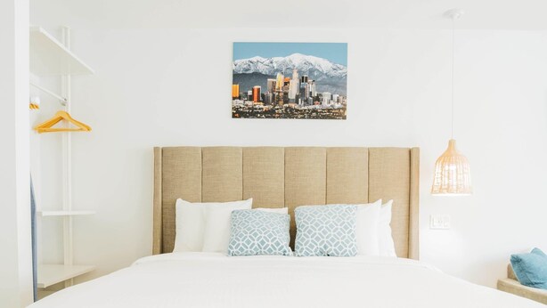 A hotel room with a large bed, a cityscape picture on the wall, a hanging light fixture, and a white wardrobe. - SKS - Superior Room, 1 King Bed with Sofa bed, Non Smoking (Long Beach)