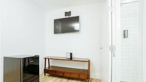 A room with a wooden floor, a built-in wooden bench, a wall-mounted flat-screen TV, and a door with a metal handle. - DQ -  Deluxe Room, 1 Queen Bed, Non Smoking (Long Beach)