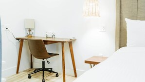 A hotel room with a wooden desk, a chair, a bed, a bedside table, a lamp, and a hanging light fixture. - DQ -  Deluxe Room, 1 Queen Bed, Non Smoking (Long Beach)