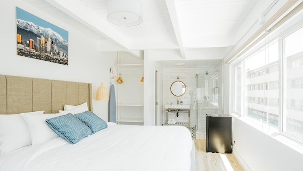 A modern hotel room with a large bed, a cityscape painting, a walk-in closet, and a bathroom with a large window. - DK - Deluxe Room, 1 King Bed, Non Smoking (Long Beach)