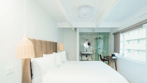 A bedroom with a large bed, a bedside table, a hanging light fixture, and a view of a bathroom with a glass shower enclosure. - DK - Deluxe Room, 1 King Bed, Non Smoking (Long Beach)