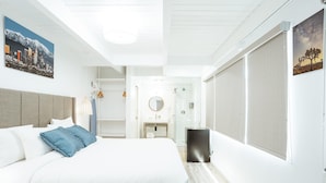 A modern hotel room with a large bed, a bedside table, a mirror, and a view of the cityscape through the window. - DK - Deluxe Room, 1 King Bed, Non Smoking (Long Beach)