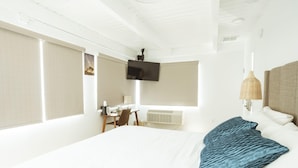 A hotel room with a large bed, a desk, a television, and a window with blinds. - DK - Deluxe Room, 1 King Bed, Non Smoking (Long Beach)