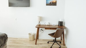 A small, tidy room with a wooden desk, a chair, a television mounted on the wall, and a picture of a sunset. - ADA - Deluxe Room, 1 Queen Bed, Accessible Non Smoking (Long Beach)