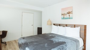 A bedroom with a bed, a desk, a chair, a door, and a wall-mounted lamp. - ADA - Deluxe Room, 1 Queen Bed, Accessible Non Smoking (Long Beach)