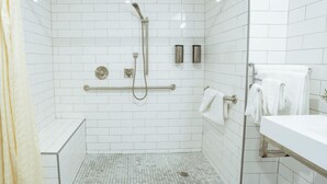 A modern bathroom with white tiled walls, a shower with a handheld showerhead, a grab bar, and a white sink with a towel rack. - ADA - Deluxe Room, 1 Queen Bed, Accessible Non Smoking (Long Beach)