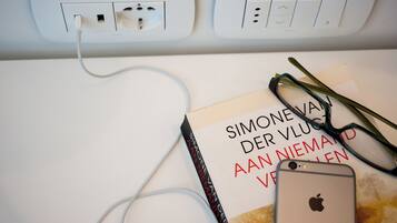 Una pared blanca con un enchufe y un interruptor. Un libro titulado "SIMONE VAN DER VLUCH" y un par de gafas están sobre la pared.