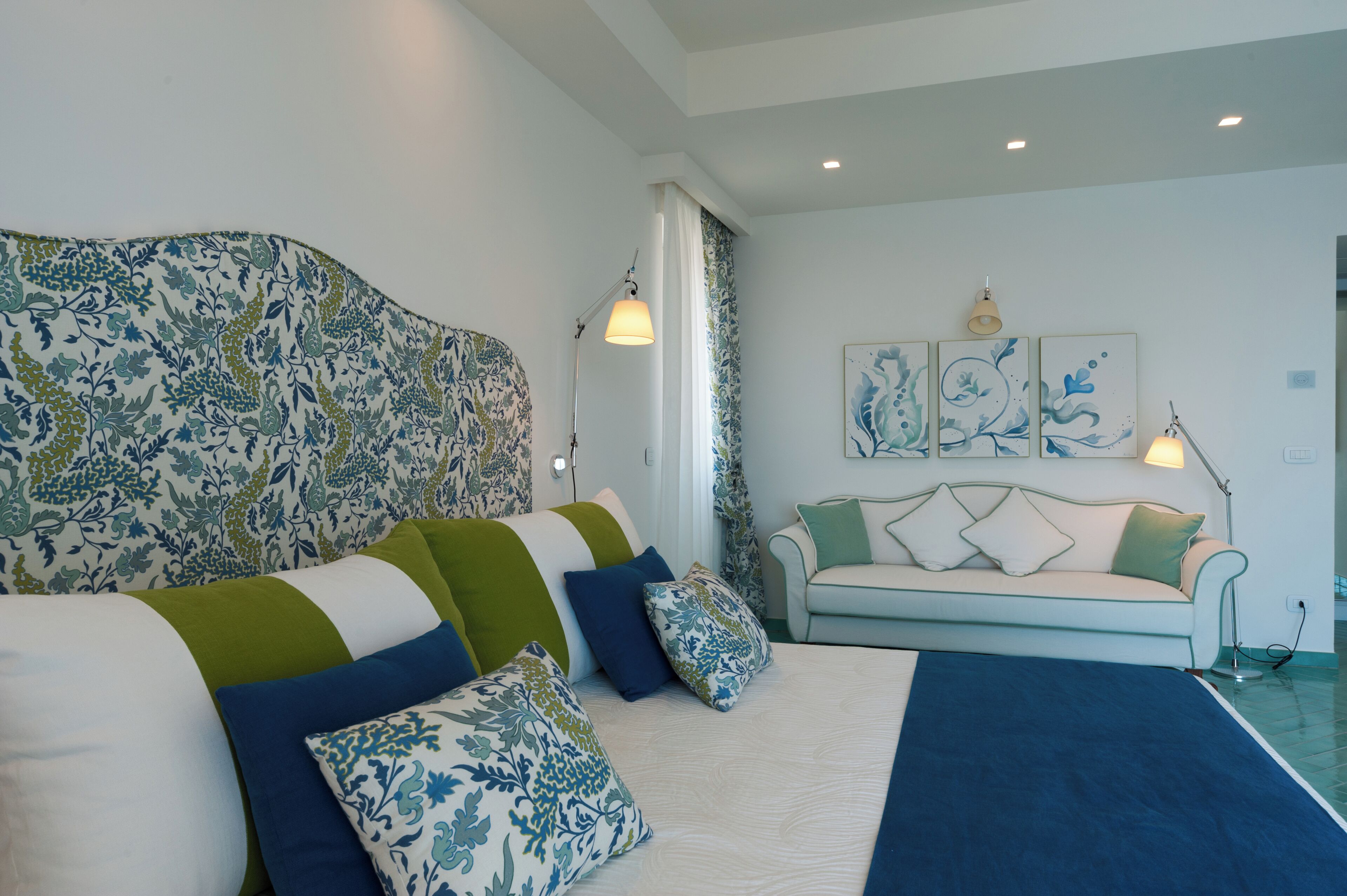 A bedroom with a large bed, a sofa, and two wall-mounted lamps.