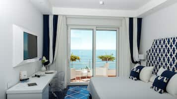 Una camera d'albergo con un letto, una scrivania, una televisione e un balcone vista mare.