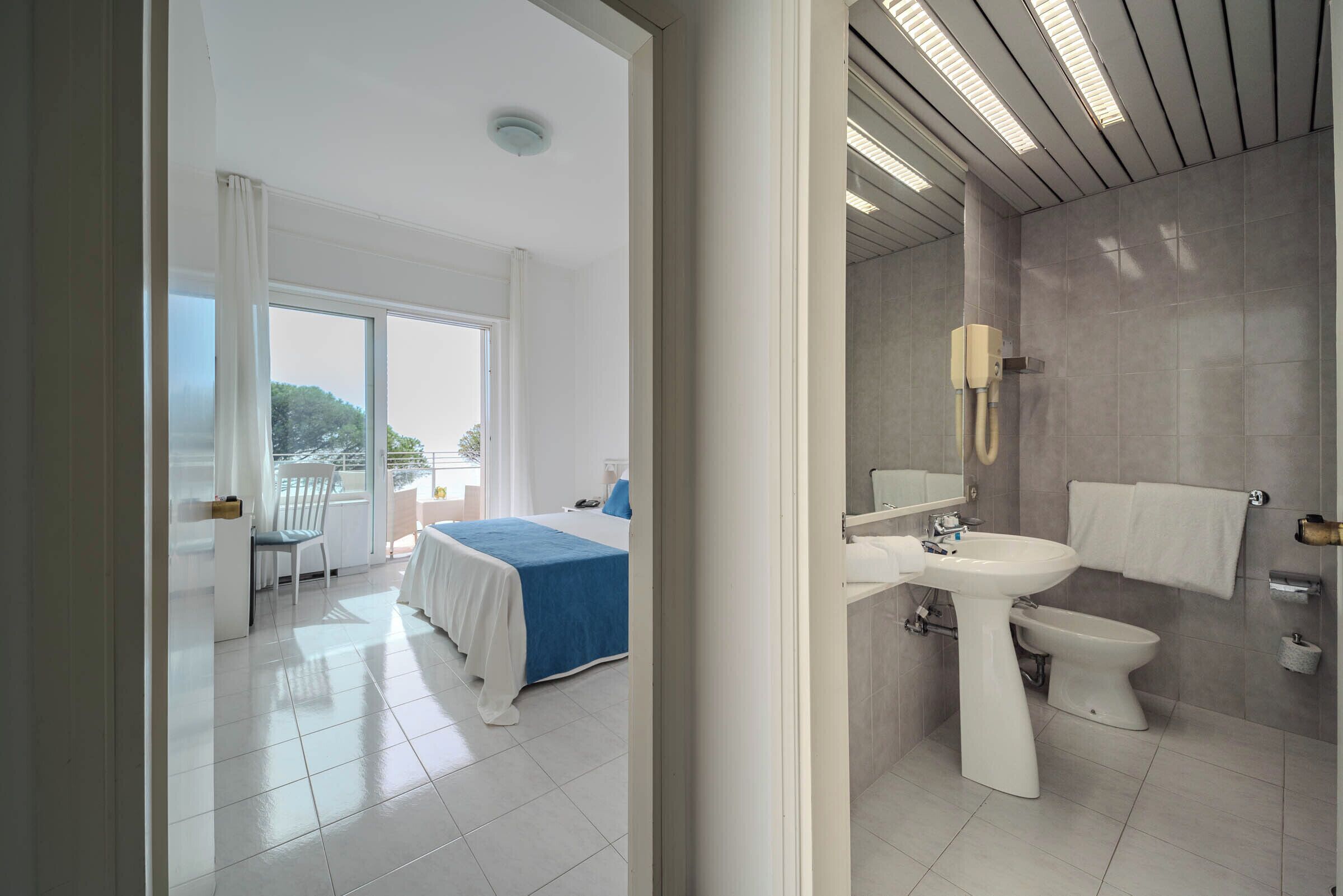A modern hotel room with a balcony, a large bed, a bathroom with a sink and toilet, and a view of the outdoors.