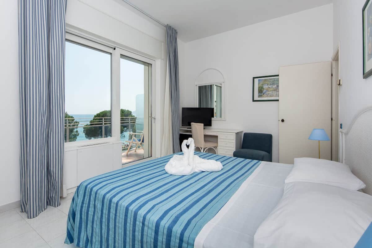 Ein Hotelzimmer mit Bett, Schreibtisch, Stuhl, Fernseher und Meerblick.
