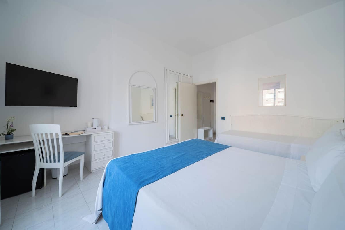 Ein Schlafzimmer mit Bett, Schreibtisch, Stuhl, Fernseher und Fenster.
